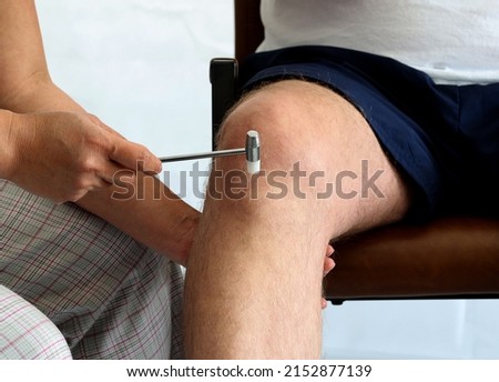 The neurologist testing knee reflex. Closeup neuropathologist doctor examination nerve reflexes with a neurological hammer checks the reflex on the knee joint on adult man's leg. 
