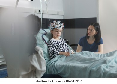 Neurology Specialist Examining Neurological Disease State Of Ill Kid. Hospitalized Sick Girl Wearing EEG Headset Resting In Patient Bed While Doctor Analyzing Brain Condition.