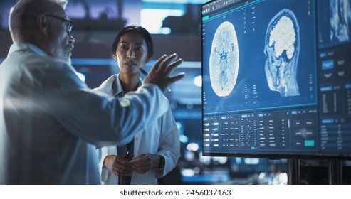 Neuroscience Laboratory Meeting: Female Asian Scientist And Male Surgeon Discussing MRI Brain Scan On TV Display. Specialists Working On Medication For Rehabilitation After Brain Damage - Powered by Shutterstock