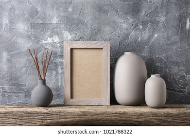 Neutral Colored Vases And Shabby Photoframe On Distressed Wooden Shelf Against Rough Plaster Grey Wall. Home Decor.