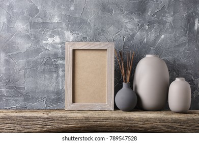 Neutral Colored Vases And Shabby Photoframe On Distressed Wooden Shelf Against Rough Plaster Grey Wall. Home Decor.