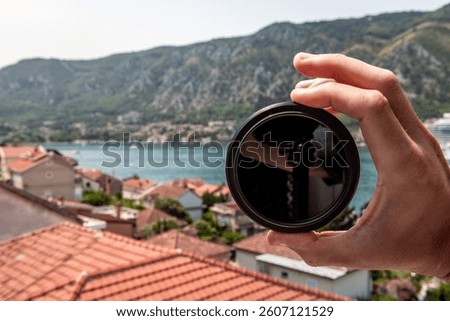Neutral density nd filter for camera lens hand holding macro closeup outside in Kotor, Montenegro with landscape nature view