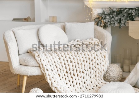 Neutral white boucle sofa with chunky knitted blanket with soft pillows in a cozy festive living room. Design of bright minimal scandinavian interior decorated round and square cushion on couch