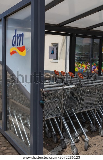 Neuwied, Germany - June 20, 2021: logo of the german\
retail drugstore chain dm on a vitreous divider wall with shopping\
carts in a row. 