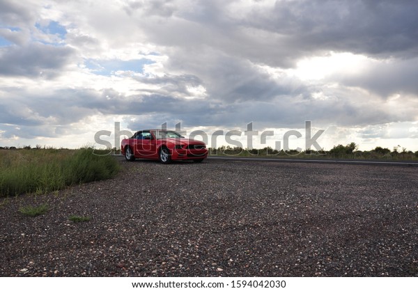 Nevada / USA - 02.10.14: red\
Dodge Challenger muscle car at sunset on gravel and asphalt\
road