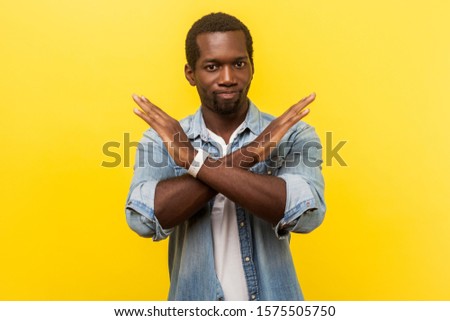 Never again. Portrait of absolutely convinced man in denim casual shirt standing crossing hands, showing x sign meaning stop, there is no way, finish. indoor studio shot isolated on yellow background