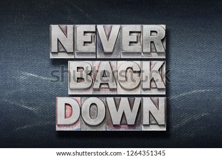 never back down phrase made from metallic letterpress on dark jeans background