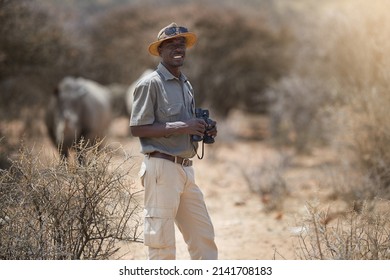 Never A Dull Moment On The Job. Portrait Of A Confident Game Ranger Looking At A Group Of Rhinos In The Veld.