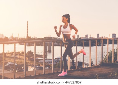 Never Give Up And Keep Moving! Full Length Of Beautiful Young Woman In Sports Clothing Running Along The Bridge 