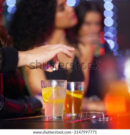 Never leave your drink alone. Closeup shot of a man drugging a womans drink in a nightclub.