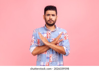 Never, no compromise! Portrait of dissatisfied bearded man in blue shirt crossing hands, showing x sign, ban or prohibition gesture, rejecting offer. Indoor studio shirt isolated on pink background.