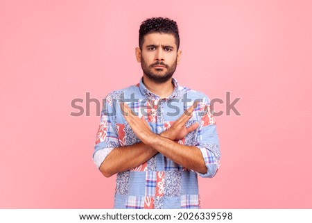 Never, no compromise! Portrait of dissatisfied bearded man in blue shirt crossing hands, showing x sign, ban or prohibition gesture, rejecting offer. Indoor studio shirt isolated on pink background.