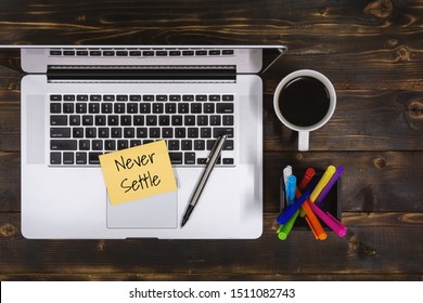 Never Settle. Overhead view of Sticky Note and Laptop on Rustic Wood.