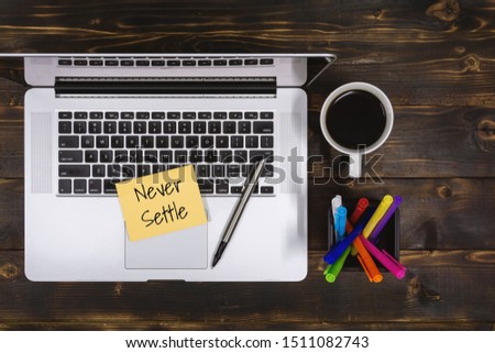 Never Settle. Overhead view of Sticky Note and Laptop on Rustic Wood.