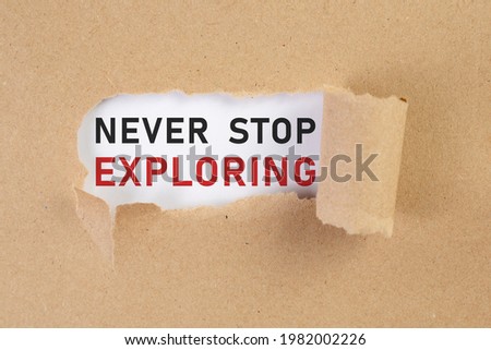 Never stop exploring, text on white paper on ripped paper background.