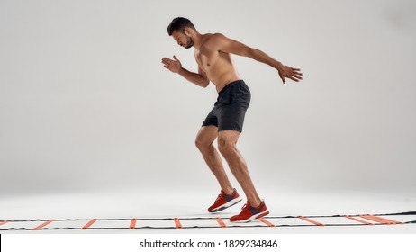 Never Stop. Full Length Shot Of Young Athletic Man Training On Agility Ladder Drill Isolated Over Grey Background. Fitness, Sport And Workout Concept