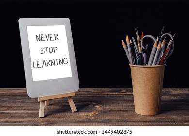 Never stop learning is written on a white sign. A wooden stand holds a white tablet and a cup of pencils