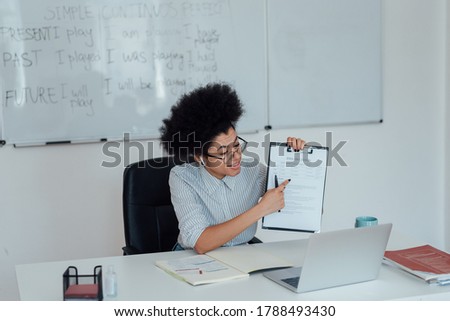 Never stop learning. Young afro american female teacher sitting at her workplace at home and explaining rules of English grammar while teaching online. Focus on a woman. E-learning. Distance education