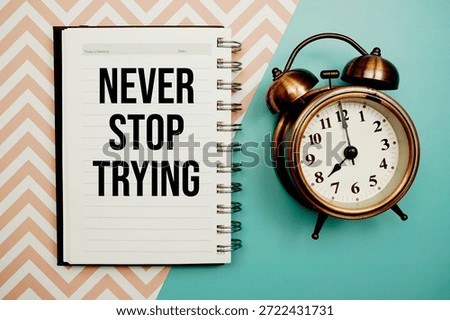 Never Stop Trying text written on notepad with alarm clock