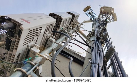 New 5G Radio Network Telecommunication Equipment With Radio Modules And Smart Antennas Mounted On A Metal Tower Radiating Strong Signal Waves Over The Dense Urban City From The Roof Of The Building 