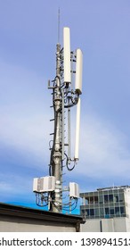 New 5G Radio Network Telecommunication Equipment With Radio Modules And Smart Antennas Mounted On A Metal Tower Radiating Strong Signal Waves Over The Dense Urban City From The Roof Of The Building 