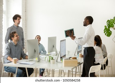 New african employee unpacking boxes and talking to friendly colleagues on first working day in office, smiling happy black worker having pleasant conversation with coworkers showing photo in frame - Powered by Shutterstock