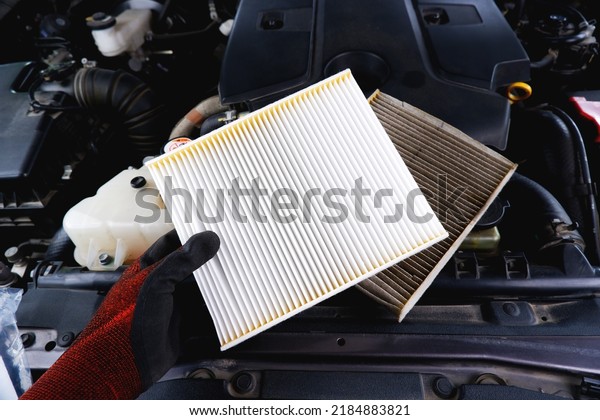 New air filter in a hand and old filthy filter\
placed on the car engine compartment, Automobile maintenance\
service business concept