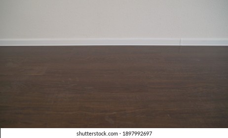 The New Apartment Has Black Laminate And White Basement. New And Empty Apartment With Wooden Floor, White Walls. Close Up Of White Plastic Baseboards On Dark Oak Wood Flooring.