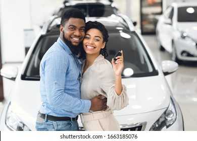 New Automobile. Cheerful Spouses Posing Hugging And Holding New Car Key In Dealership Showroom.