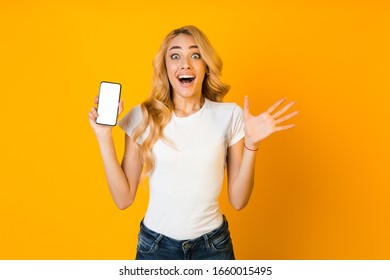 New awesome application. Surprised girl showing phone with blank screen over yellow studio background - Shutterstock ID 1660015495