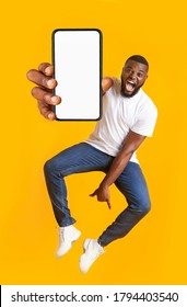 New Awesome Mobile App. Closeup Of Smartphone With Blank Screen In Jumping Emotional Black Guy Hand, Yellow Studio Background