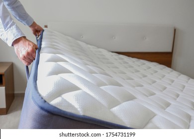 New Bed Delivery And Assembly Service Concept. Cropped Shot Of Male Worker's Hands In Process Of Laying The Orthopedic Foam Mattress On Carcass In Customer's Bedroom. Close Up, Copy Space, Background.