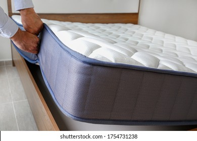 New Bed Delivery And Assembly Service Concept. Cropped Shot Of Male Worker's Hands In Process Of Laying The Orthopedic Foam Mattress On Carcass In Customer's Bedroom. Close Up, Copy Space, Background.