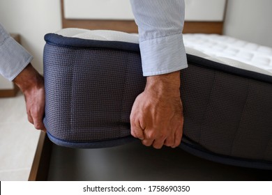 New Bed Delivery And Assembly Service Concept. Cropped Shot Of Male Worker's Hands In Process Of Laying The Orthopedic Foam Mattress On Carcass In Customer's Bedroom. Close Up, Copy Space, Background.