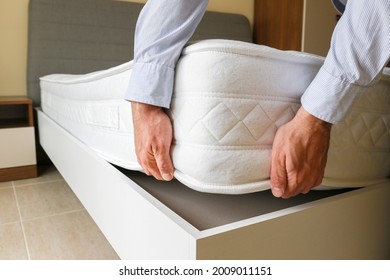 New Bed Delivery And Assembly Service Concept. Cropped Shot Of Male Worker's Hands In Process Of Laying The Orthopedic Foam Mattress On Carcass In Customer's Bedroom. Close Up, Copy Space, Background.