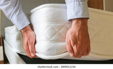 New Bed Delivery And Assembly Service Concept. Cropped Shot Of Male Worker's Hands In Process Of Laying The Orthopedic Foam Mattress On Carcass In Customer's Bedroom. Close Up, Copy Space, Background.