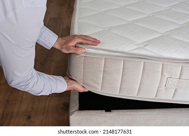 New Bed Delivery And Assembly Service Concept. Cropped Shot Of Male Worker's Hands In Process Of Laying The Orthopedic Foam Mattress On Carcass In Customer's Bedroom. Close Up, Copy Space, Background.