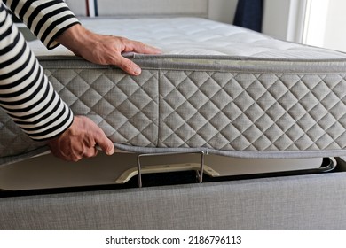 New Bed Delivery And Assembly Service Concept. Cropped Shot Of Male Worker's Hands In Process Of Laying The Orthopedic Foam Mattress On Carcass In Customer's Bedroom. Close Up, Copy Space, Background.