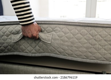 New Bed Delivery And Assembly Service Concept. Cropped Shot Of Male Worker's Hands In Process Of Laying The Orthopedic Foam Mattress On Carcass In Customer's Bedroom. Close Up, Copy Space, Background.