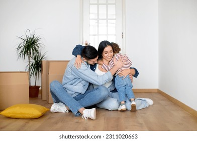 New Beginnings. Happy Family Of Three Embracing At Home On Moving Day, Cheerful Young Parents And Child Hugging While Sitting On Floor Among Cardboard Boxes, Celebrting Relocation To New Flat - Shutterstock ID 2311020663
