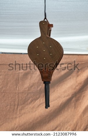 An new bellows made in leather and wood. The bellows is rested on a wall of bricks and an a brown background.
