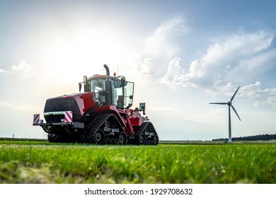New big red modern farm tractor with quad tracks for powerful combine trailer and ploughing attachments.  Parked in sunshine on farmers rural agricultural field with wind turbine electric generator.