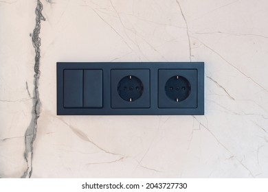 New black switch and socket on the marble wall. Kitchen background. Electric light switch and socket on the empty wall. Electrical power socket and plug switched.