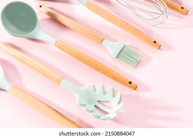 New Blue Silicone Kitchen Utensils With Wooden Handles On A Pink Background.