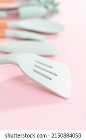 New Blue Silicone Kitchen Utensils With Wooden Handles On A Pink Background.