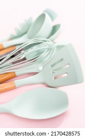 New Blue Silicone Kitchen Utensils With Wooden Handles On A Pink Background.