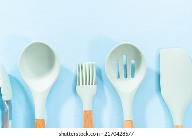 New Blue Silicone Kitchen Utensils With Wooden Handles On A Blue Background.