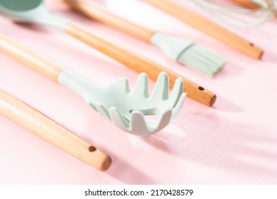 New Blue Silicone Kitchen Utensils With Wooden Handles On A Pink Background.