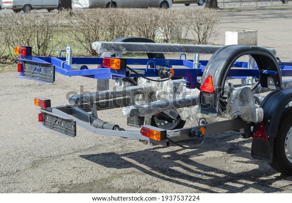 New boat trailers for\
sale. Rear of vehicles with reflectors. Outdoors. City traffic in\
the background.