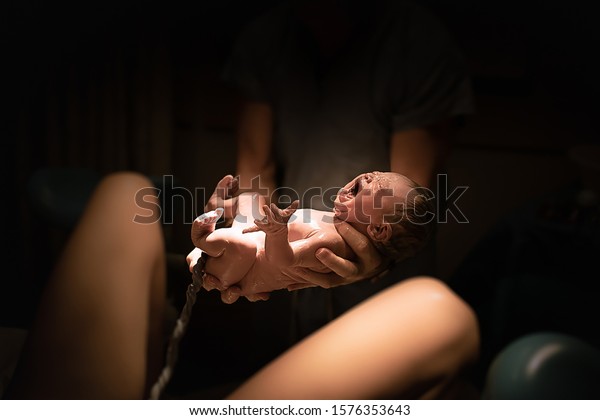 New born baby girl first moments out of her\
mothers womb. New life\
concept.